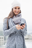 Cheerful woman with winter clothes on text messaging