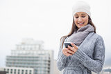 Smiling young woman with winter clothes on text messaging