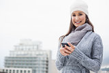 Cheerful young woman with winter clothes on text messaging