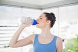 Pretty fit woman drinking water on her plastic flask