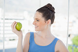 Smiling slender woman in sportswear holding green apple