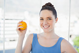 Smiling slender woman in sportswear holding orange