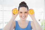 Cheerful slender woman in sportswear holding slices of orange