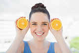 Smiling slender woman in sportswear holding slices of orange