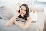Smiling cute woman lying on a cosy couch having a phone call