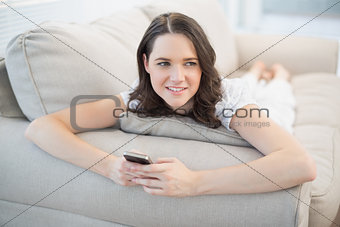 Cheerful cute woman lying on a cosy couch sending text message