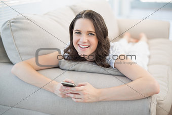 Cheerful pretty woman lying on a cosy couch sending text message