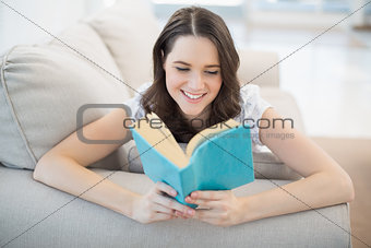 Peaceful pretty woman lying on a cosy couch reading book