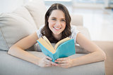 Peaceful cute woman lying on a cosy couch reading book