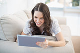 Cheerful woman lying on a cosy couch using tablet pc