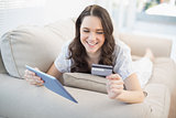 Cheerful woman lying on a cosy couch buying online