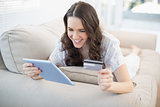 Smiling woman lying on a cosy couch buying online