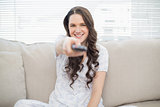 Smiling young woman holding remote sitting on a cosy couch