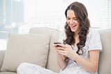 Smiling pretty woman in pyjamas reading a text on her smartphone