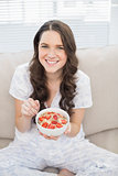Smiling pretty woman in pyjamas eating fruity cereal