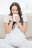 Relaxed young woman in pyjamas having coffee