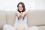 Smiling woman in pyjamas having popcorn while watching tv