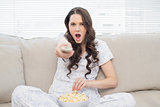 Shocked woman in pyjamas having popcorn while watching tv