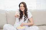 Cheerful woman in pyjamas having popcorn while watching tv