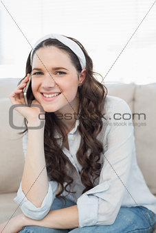 Smiling casual woman sitting on a cosy couch having a phone call