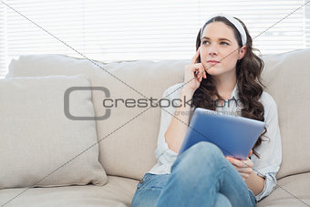 Thoughtful casual woman on cosy couch using tablet pc