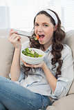 Cute casual woman on cosy couch eating salad