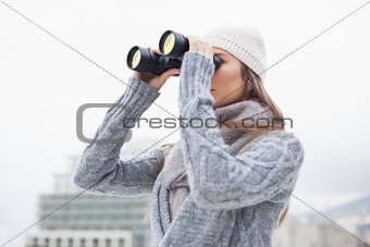 Pretty woman with winter clothes on looking through binoculars