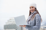 Smiling woman with winter clothes on using her laptop