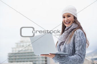 Smiling woman with winter clothes on using her laptop