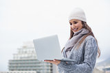 Cheerful woman with winter clothes on using her laptop