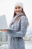 Happy woman with winter clothes on using her laptop