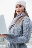 Thoughtful woman with winter clothes on using her laptop