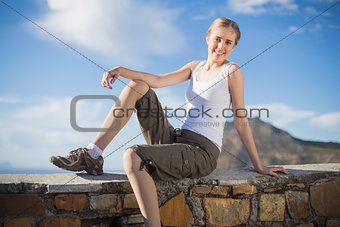 Smiling woman sitting on wall looking at camera