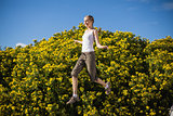 Smiling woman jumping beside yellow flowers