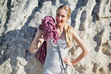 Smiling woman holding climbing equipment leaning at rock