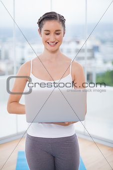 Smiling sporty brunette using her laptop