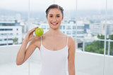 Cheerful sporty brunette holding green apple