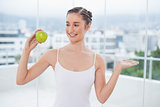 Smiling sporty brunette holding green healthy apple