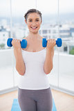 Cheerful sporty brunette exercising with dumbbells