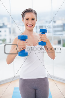 Cheerful athletic brunette exercising with dumbbells