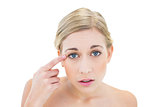 Anxious young blonde woman pointing her eye with her finger