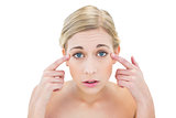 Worried young blonde woman pointing her eyes with her fingers