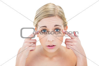 Worried young blonde woman pointing her eyes with her fingers