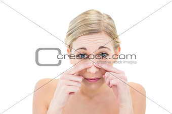 Frowning young blonde woman touching her nose