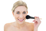 Pleased young blonde woman applying powder on her cheek