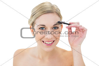 Cheerful young blonde woman brushing her eyebrow
