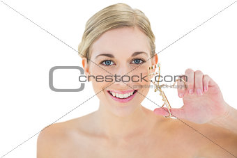 Happy young blonde woman holding eyelash curler
