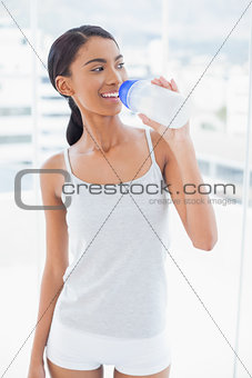 Cheerful sporty model drinking water from her flask