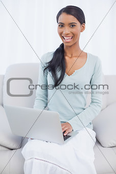 Smiling attractive woman using her laptop sitting on cosy sofa