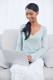 Cheerful attractive woman using her laptop sitting on cosy sofa